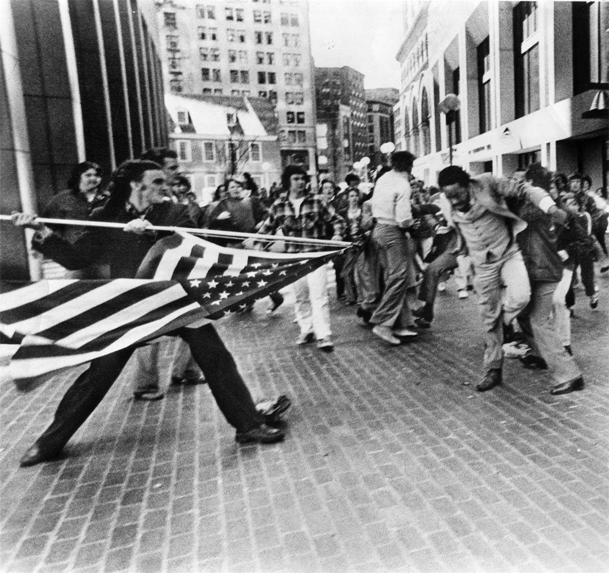 A black businessman is attacked with an American flag during an anti-busing riot.